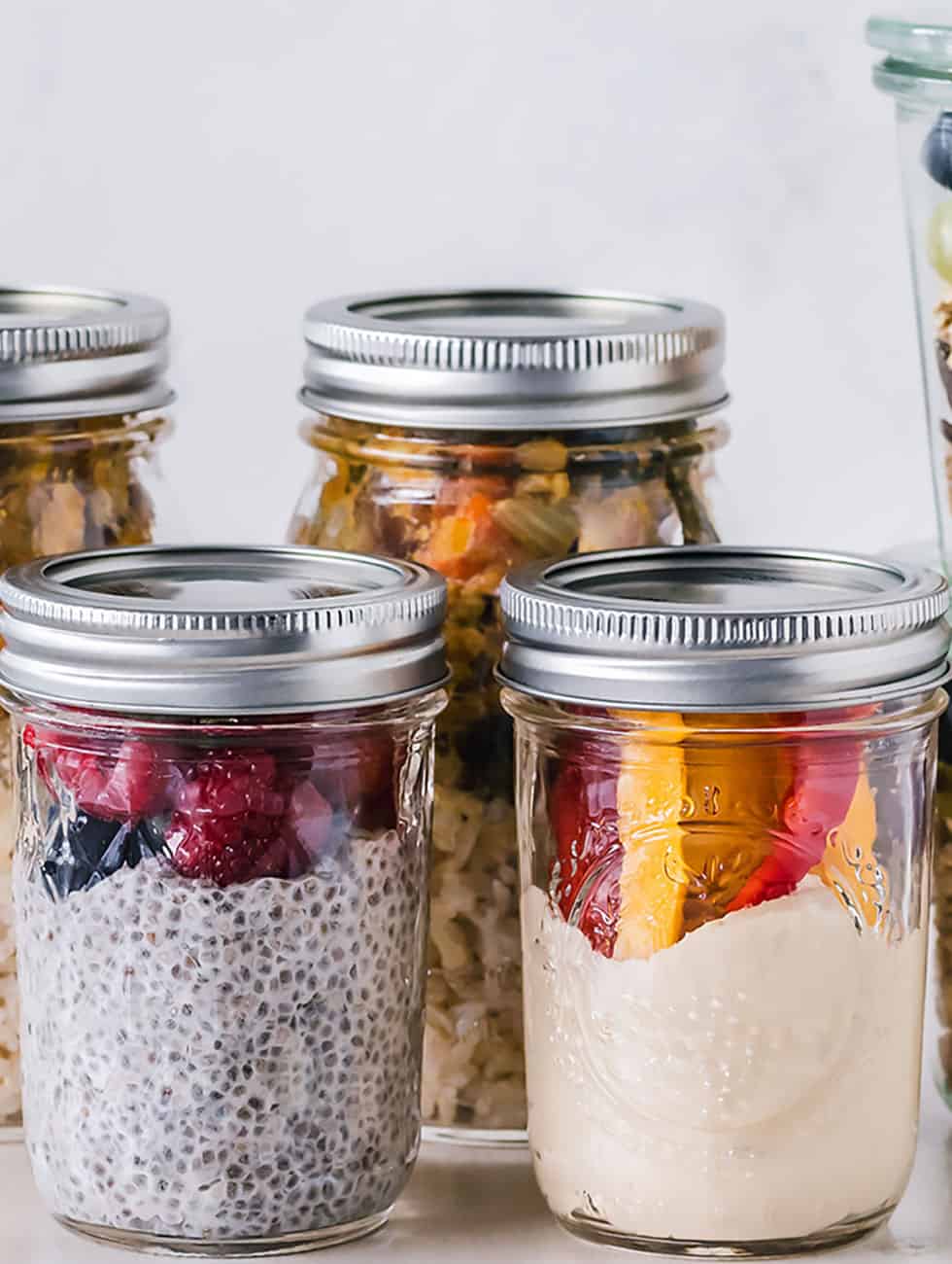 six fruit cereals in clear glass mason jars on white surface